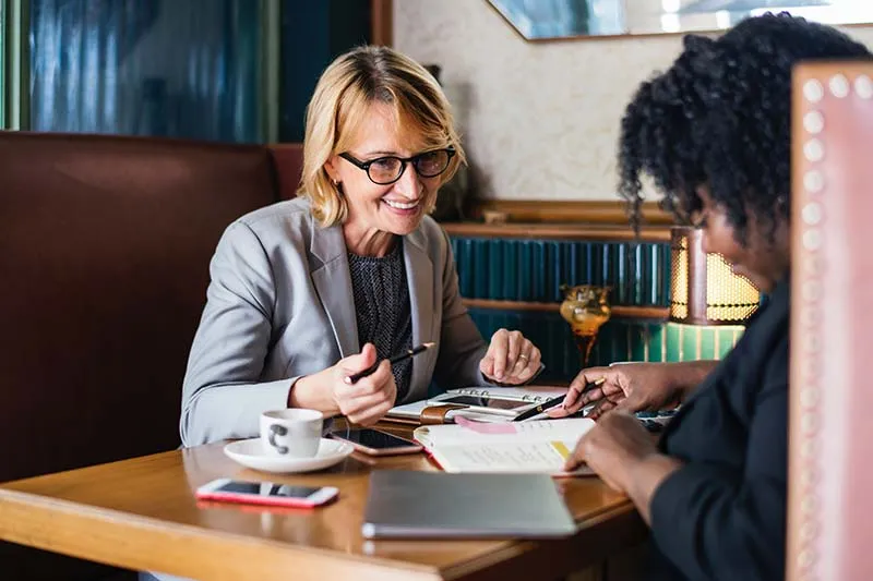 Two middle-aged women work toether on a project in a restaurant