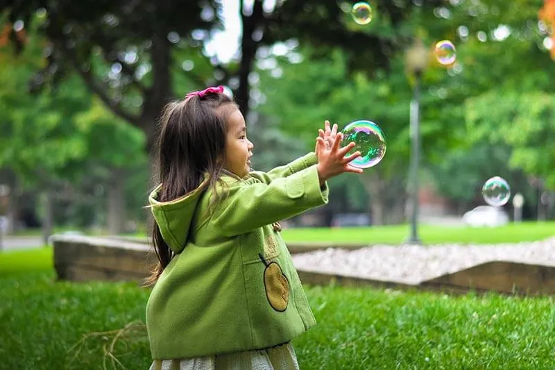 a little girl playing with soap bubbles in a park