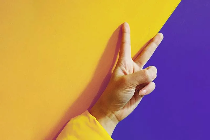 victory sign of fingers on yellow and purple wall